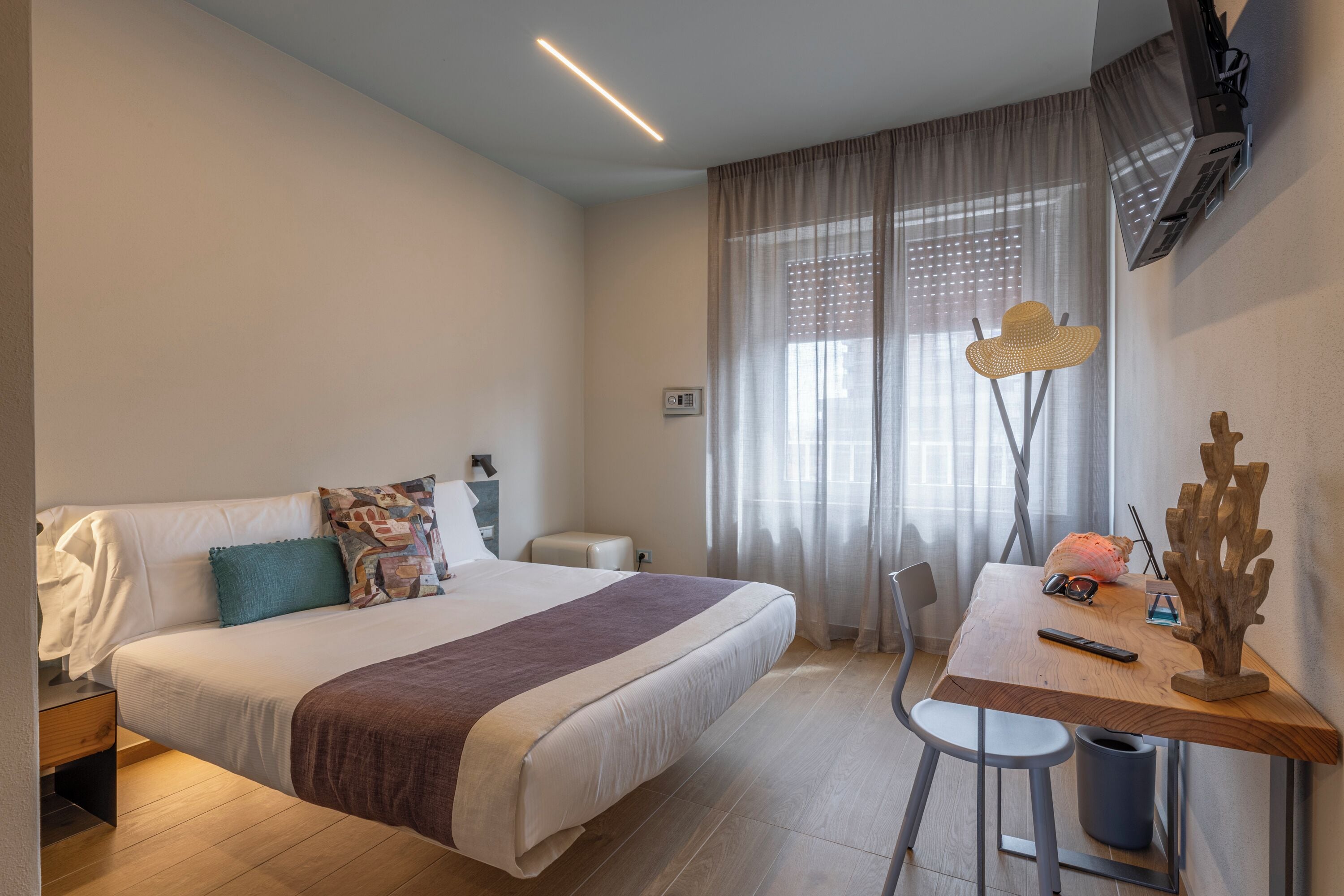 Una habitación de hotel moderna con una cama grande, un escritorio de madera y un televisor montado en la pared.