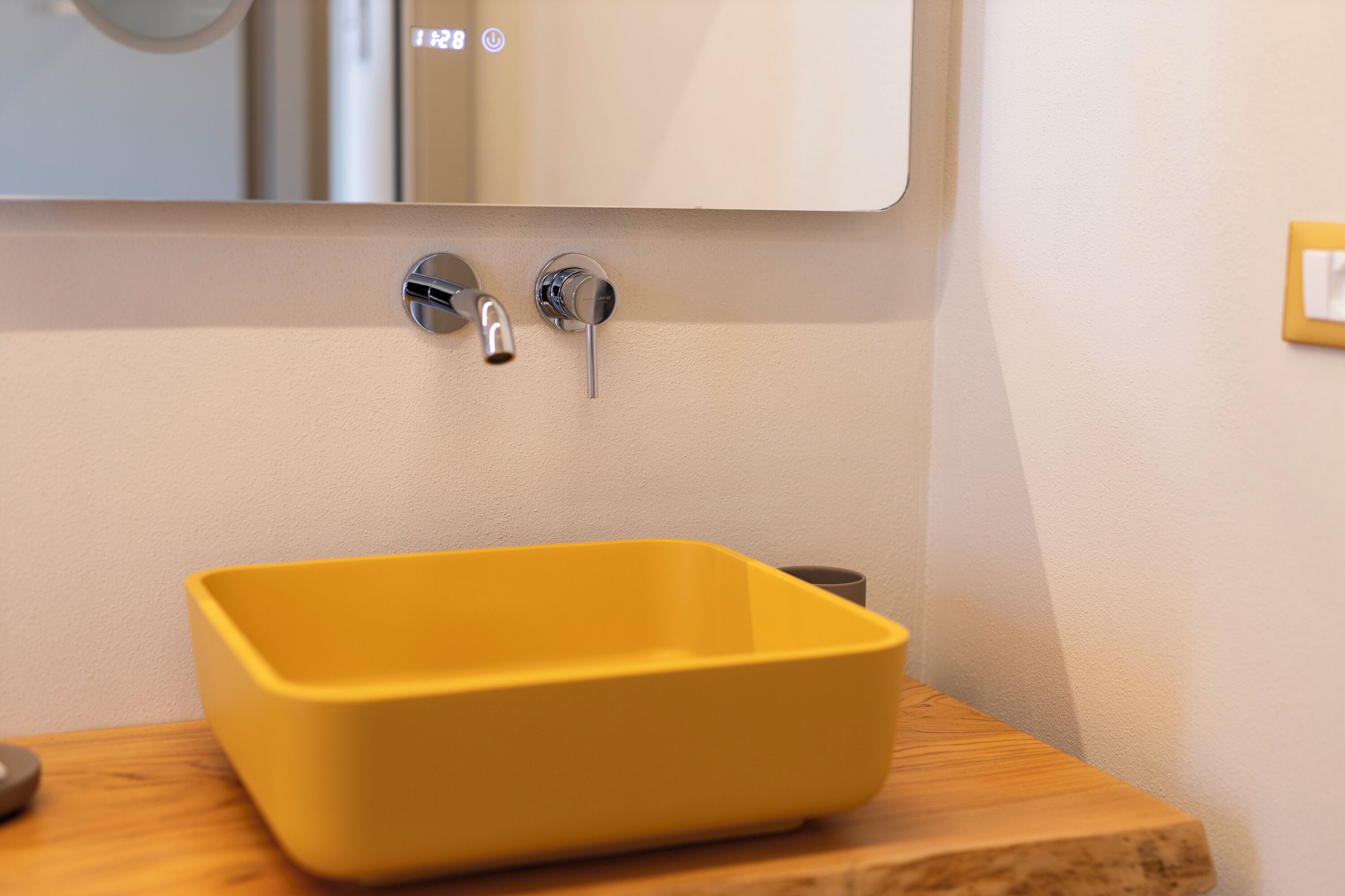 Un baño con un lavamanos amarillo, un espejo y una encimera de madera.