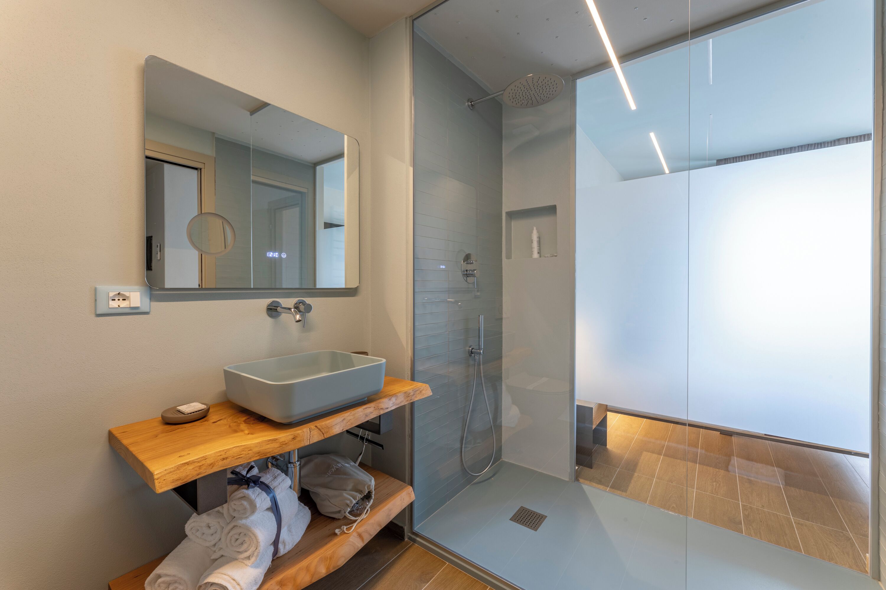 Un baño moderno con ducha de vidrio, un espejo grande y un tocador de madera con lavabo.