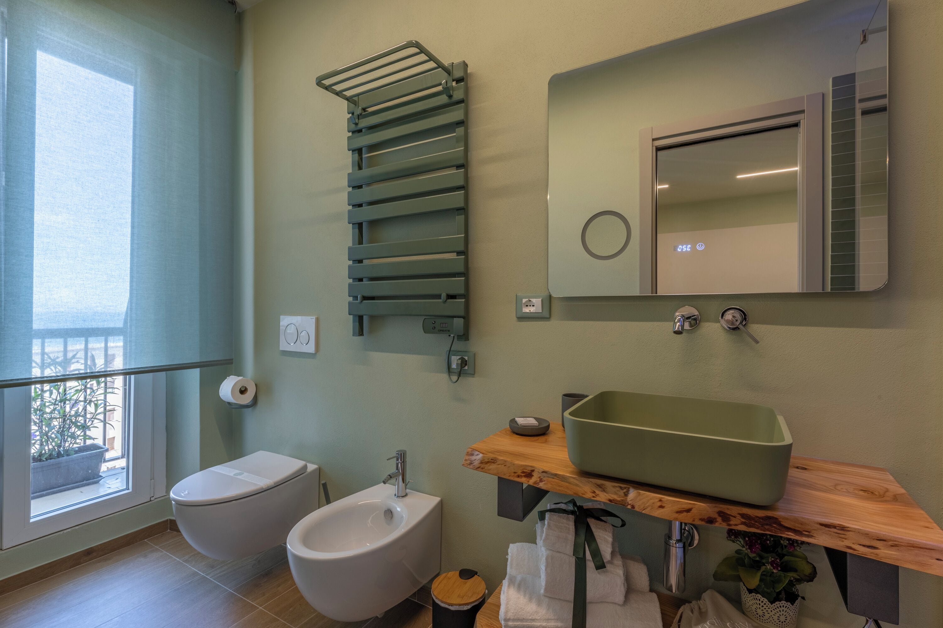 A bathroom with a toilet, bidet, and a green sink on a wooden countertop.