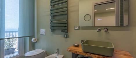 A bathroom with a toilet, bidet, and a green sink on a wooden countertop.
