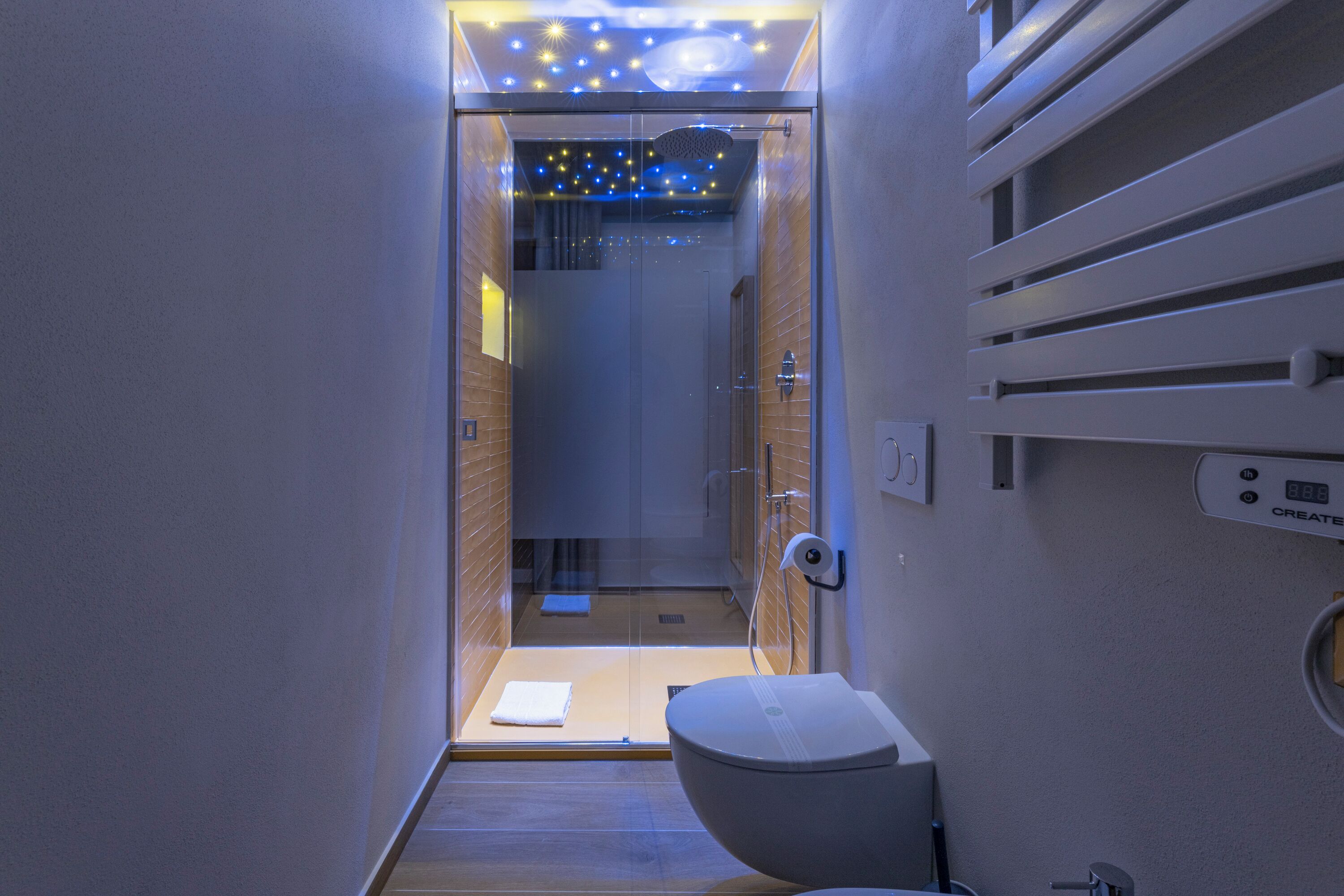 A modern bathroom with a glass shower enclosure, a toilet, and a control panel on the wall.