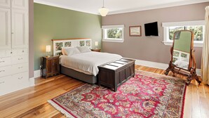 Une chambre à coucher comprenant un lit, des tables de chevet, une commode, un grand tapis, un miroir et une fenêtre.