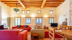 A spacious living room with wooden beams, a fireplace, and a television. - Paros VIP Pool Villa (Παροικιά)