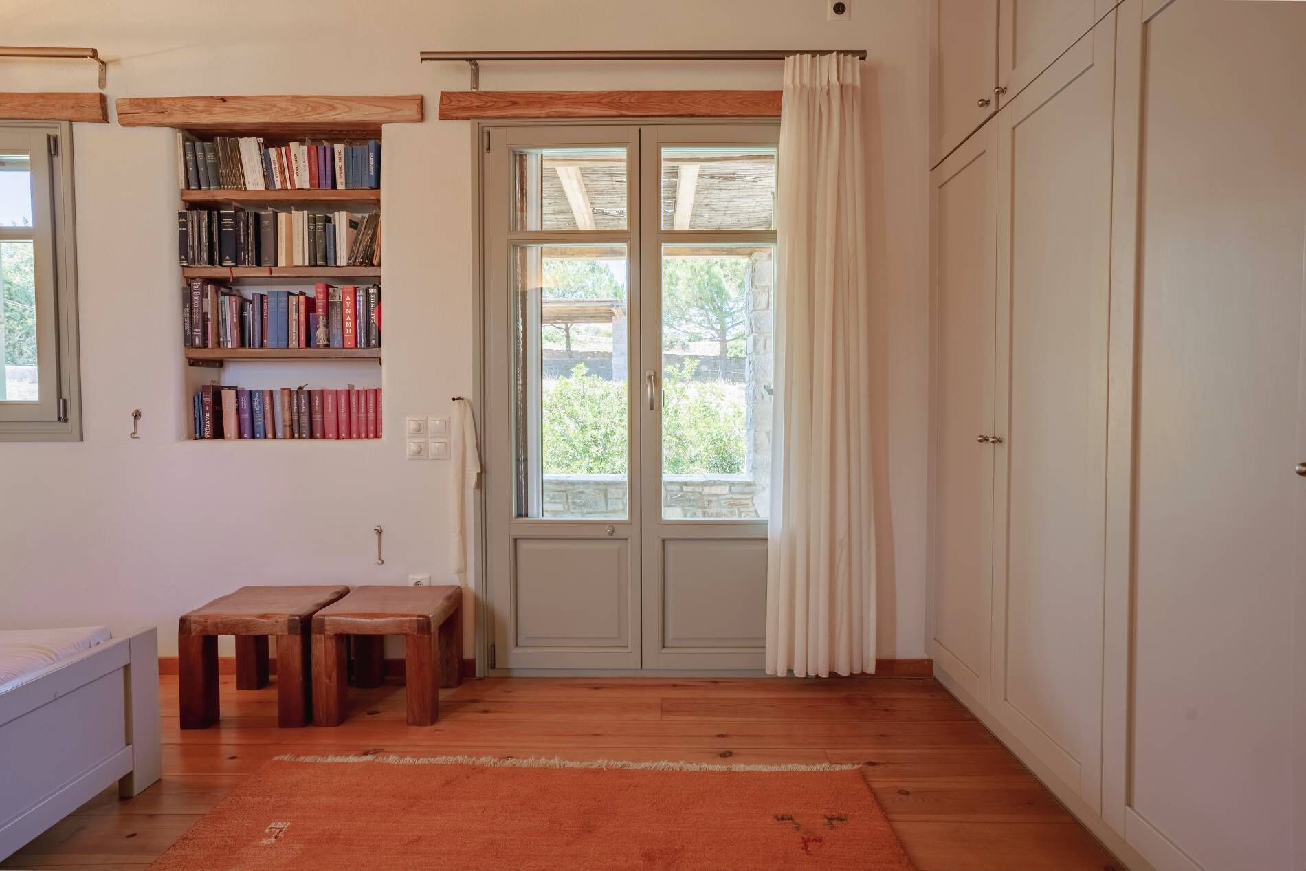 Une pièce avec un plancher en bois, une bibliothèque, un banc, une porte à panneaux de verre et une armoire.