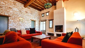 A cozy living room with stone walls, a fireplace, and red furniture. - Paros VIP Pool Villa (Παροικιά)