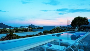A swimming pool with lounge chairs and a towel, surrounded by greenery and a view of mountains and the sea. - Paros VIP Pool Villa (Παροικιά)