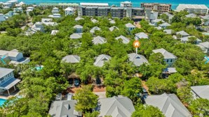 Eine Vogelperspektive zeigt ein Resort mit mehreren bungalowartigen Gebäuden, umgeben von üppiger Vegetation, einem Swimmingpool und Blick aufs Meer.