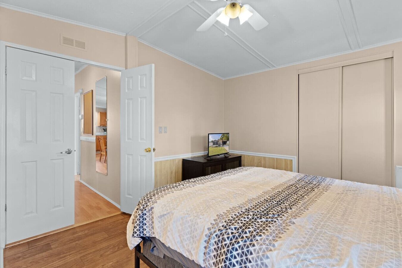 Una camera da letto con un letto, una televisione su un mobile e una porta che dà su un'altra stanza.