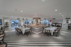 Ein geräumiger Hotel-Speisesaal mit mehreren Tischen und Stühlen, die um ein zentrales dekoratives Element angeordnet sind.