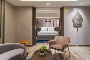 Een hotelkamer met een bed, een zithoek met een stoel en een tafel, en een decoratief kunstwerk aan de muur.