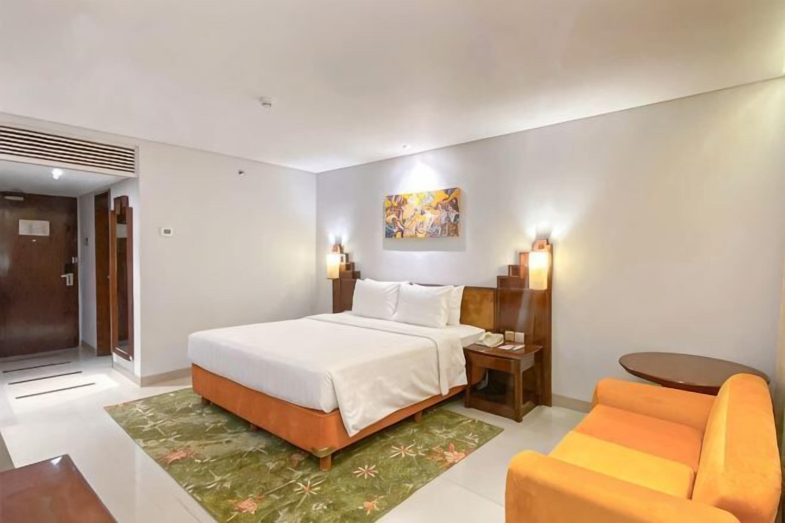 A hotel room with a bed, bedside table, lamp, and a small round table.