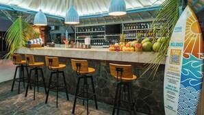 Eine Bar mit einer Theke, Barhocker, blauen Pendelleuchten und einer Surfbrett-Dekoration.