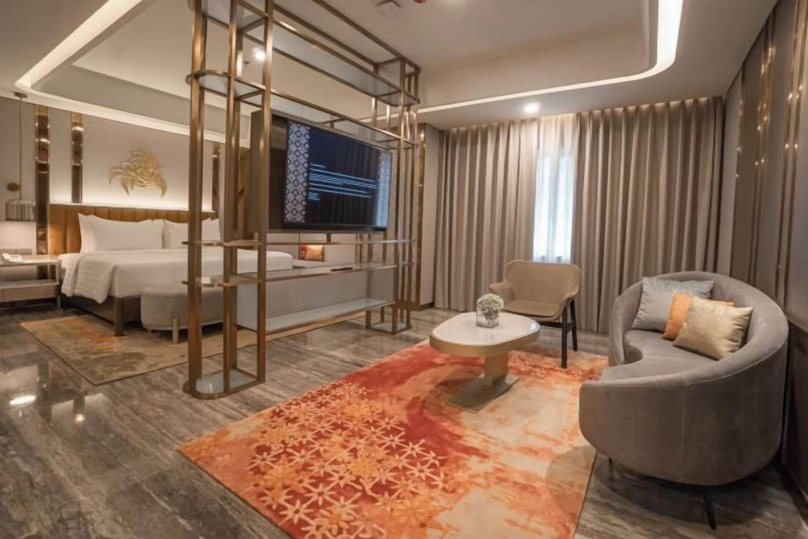 A modern hotel room with a bed, sofa, TV, and a decorative rug.