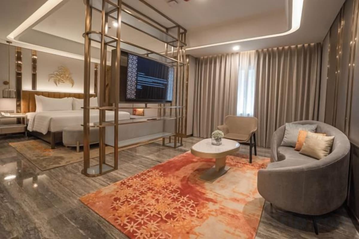 Une chambre d’hôtel moderne équipée d’un lit, d’un canapé, d’une télévision et d’un tapis décoratif.