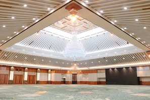 Une grande salle avec un plafond haut, un lustre et un sol recouvert de moquette.