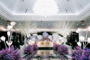 Un vaste hall orné d’un lustre, de motifs décoratifs blancs et de fleurs violettes.