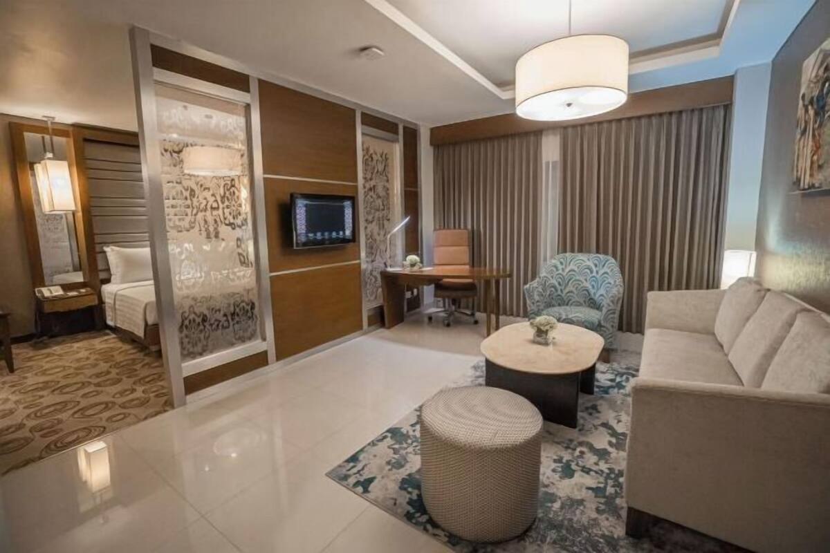 Een moderne hotelkamer met een groot bed, een bureau, een ronde salontafel, een bank en een stoel.