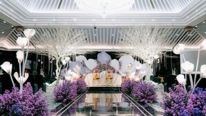Ein modernes Interieur mit einer zentralen Bühne, weißen Dekoelementen und lila Blumenarrangements.