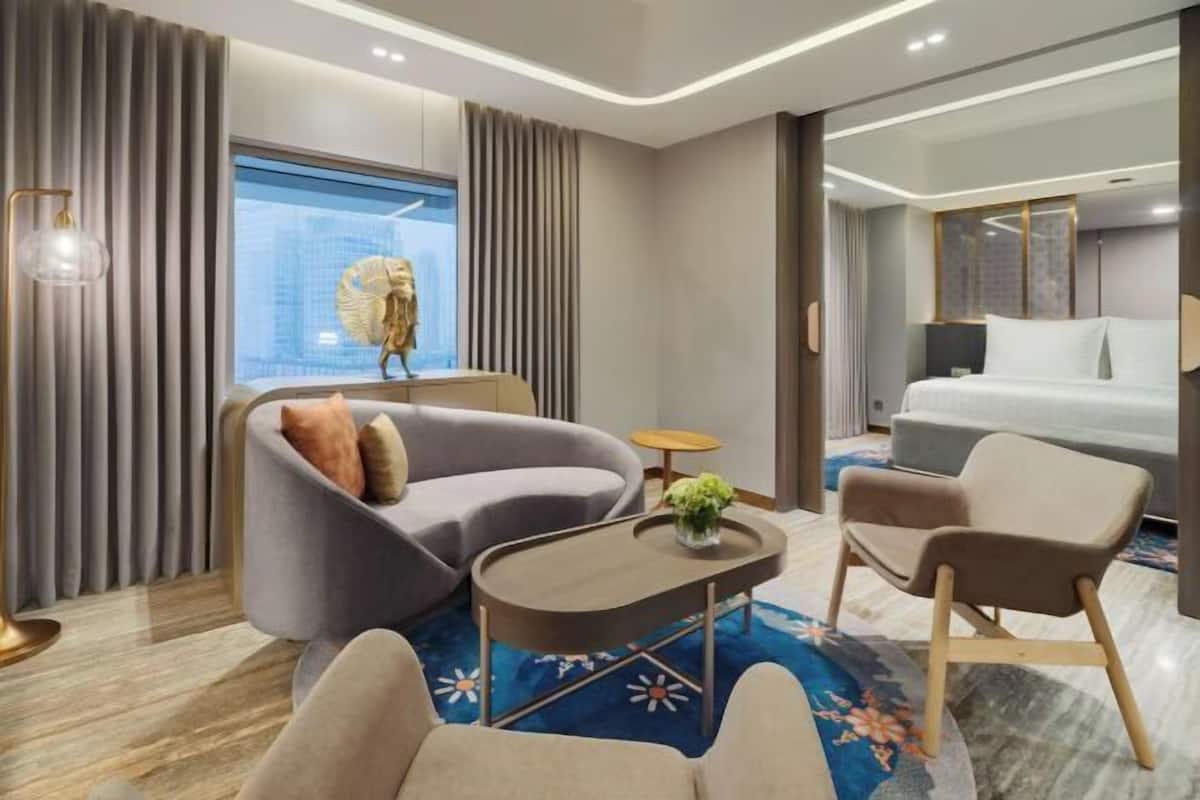 Een moderne hotelkamer met een gebogen bank, een klein rond tafeltje, een bed en een groot raam met gordijnen.