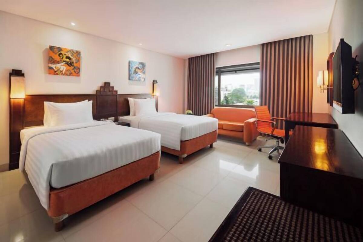 Een hotelkamer met twee bedden, een bureau, een stoel, een bank en kunstwerken aan de wanden.