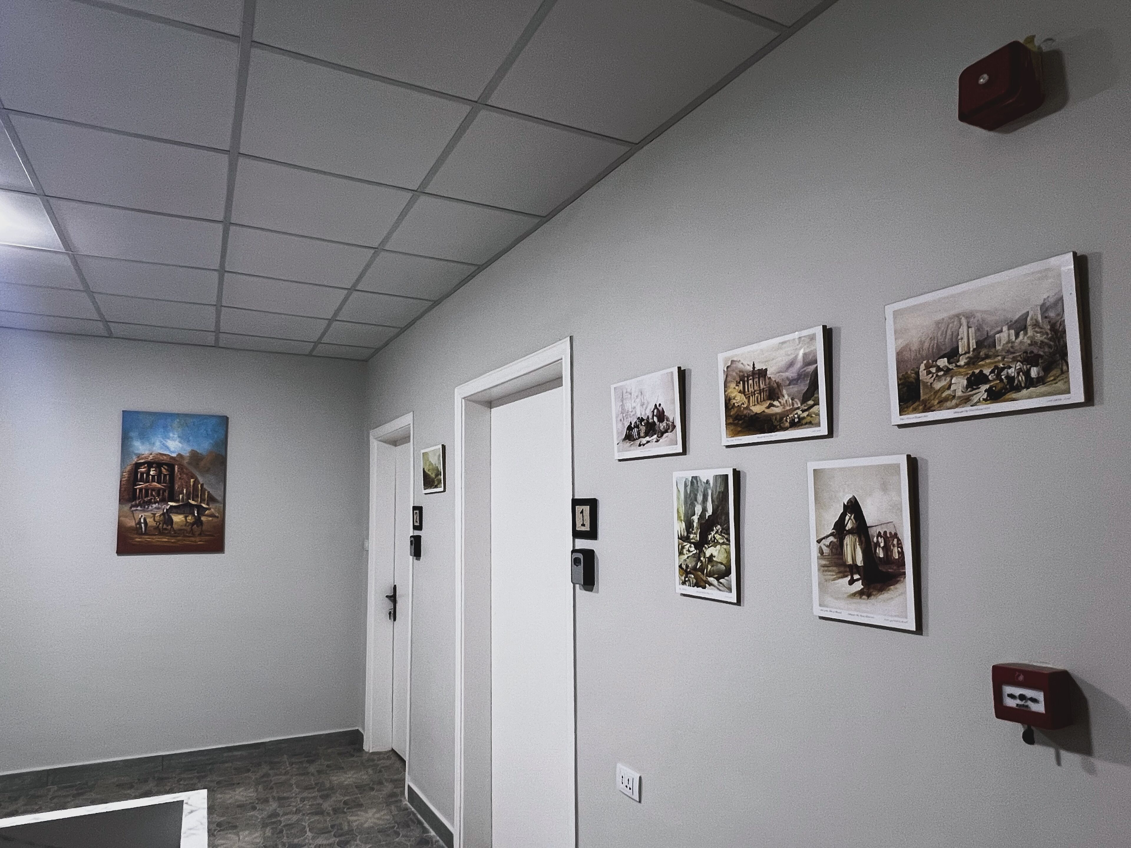 Un couloir avec un plafond recouvert de carreaux, une porte et plusieurs tableaux encadrés accrochés au mur.