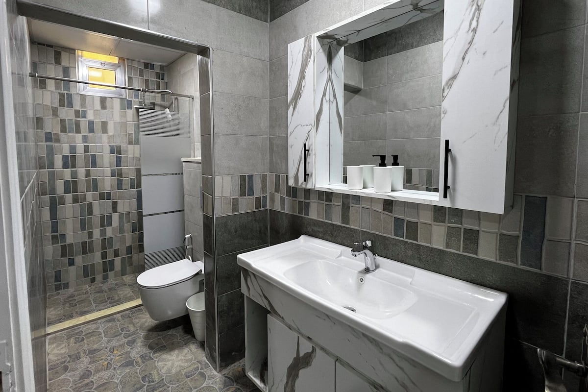 A modern bathroom with a marble sink, a toilet, and a shower area with mosaic tiles.