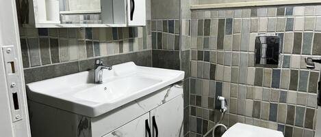 Un baño con lavamanos blanco, espejo, inodoro y zona de ducha.