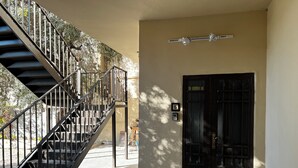 A staircase leading to a door with a number plate, a wall-mounted light fixture, and a shadow of a tree. - Downtown inn  (Madaba)