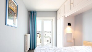 A bedroom with a bed, a radiator, a window with curtains, a wall-mounted light, and a framed picture. - Apartment met Zeezicht in Oostende (Ostend)