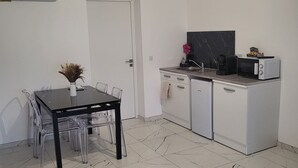 A compact kitchen with a dining table, chairs, a refrigerator, and a microwave.