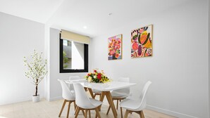 Un espace repas moderne avec une table blanche, quatre chaises blanches et un vase de fleurs.