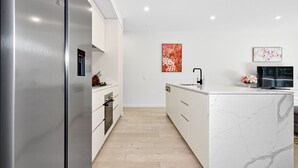 Une cuisine moderne avec des meubles blancs, un réfrigérateur en acier inoxydable et un plan de travail en marbre.