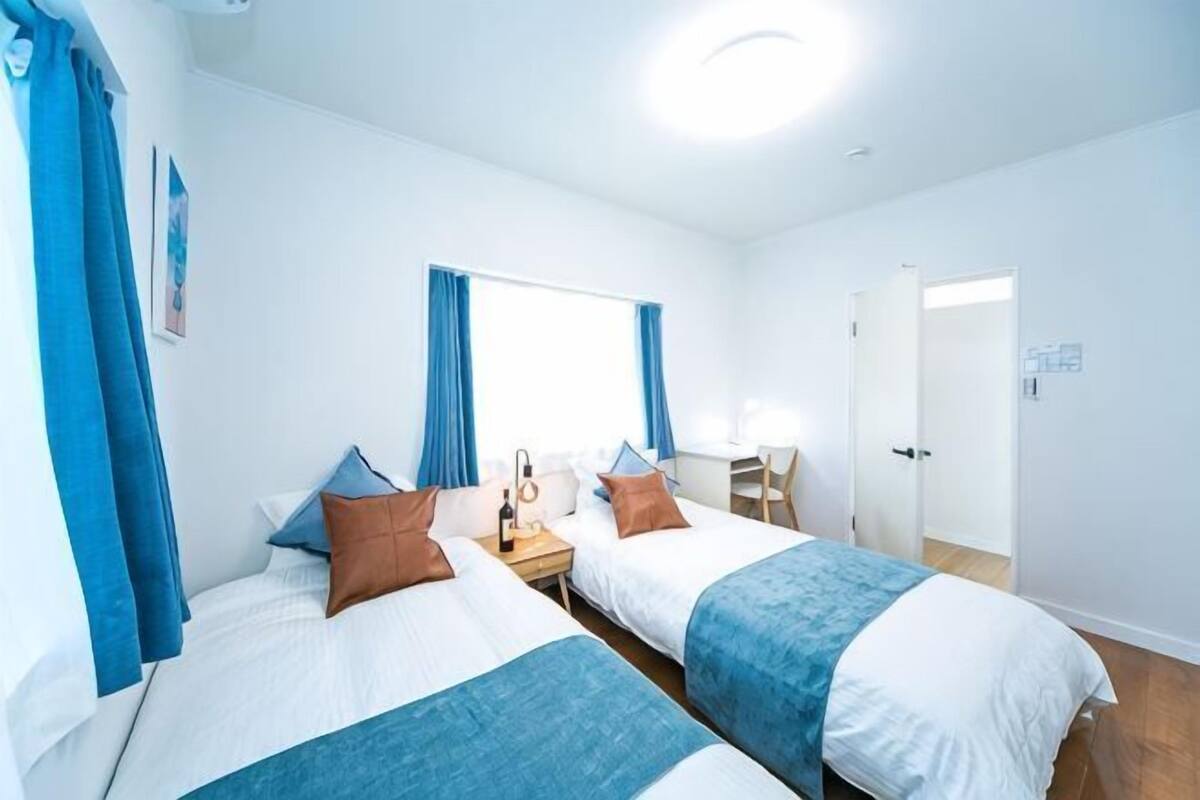 A hotel room with two beds, a desk, a chair, and a window with curtains.