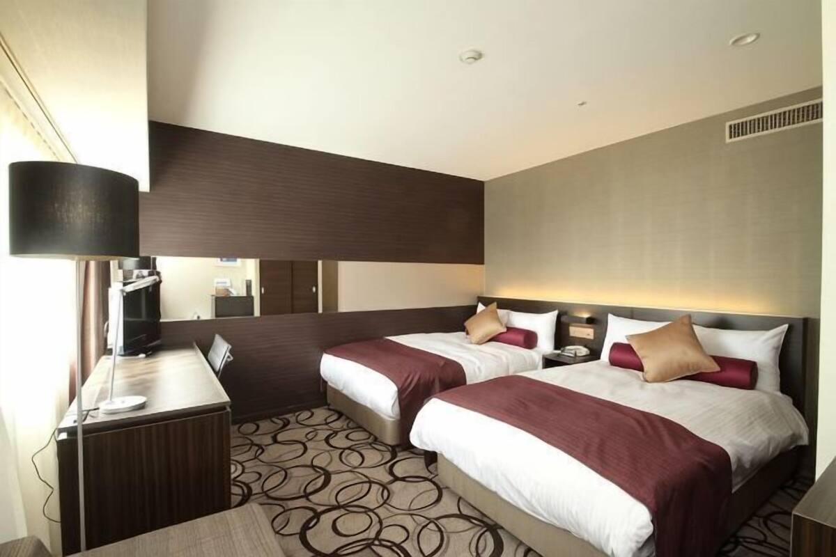 Ein Hotelzimmer mit zwei Betten, einem Schreibtisch, einer Lampe und einem Spiegel.