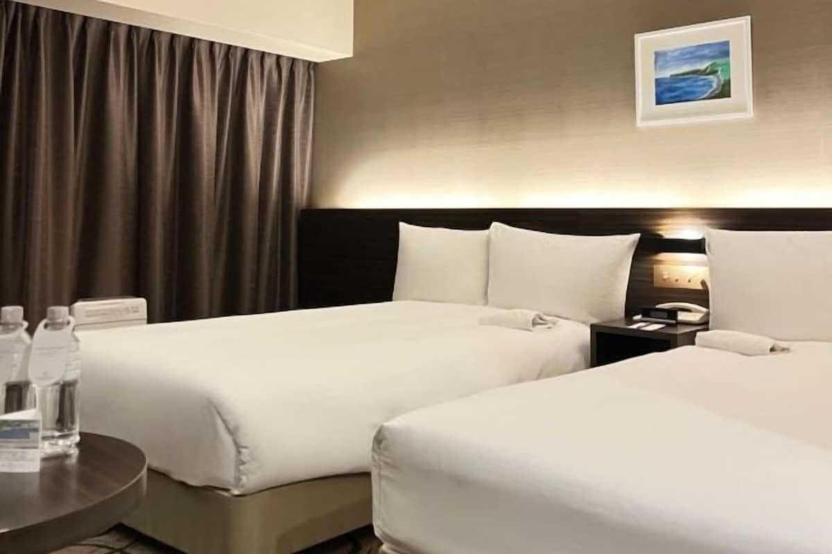 A hotel room with two beds, a nightstand, a lamp, and a painting on the wall.