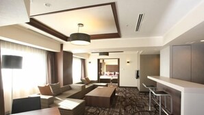 Habitación de hotel con sofá, mesa de comedor, zona de bar y dormitorio separado visible a través de una puerta abierta.