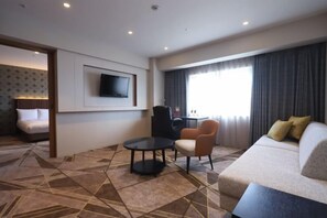A hotel room with a sofa, armchair, and a TV mounted on the wall. - ANA Crowne Plaza KUSHIRO by IHG (Kushiro City)