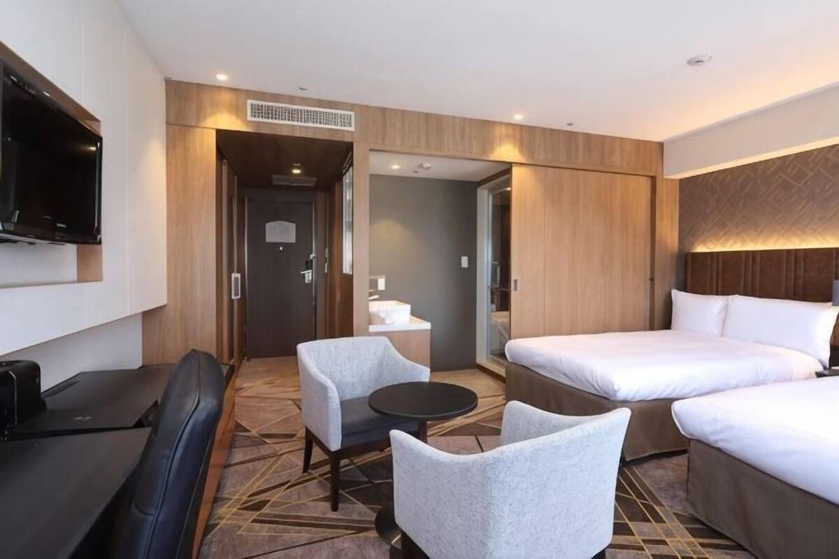 Ein Hotelzimmer mit Fernseher, zwei Betten, einer Sitzecke, einem kleinen Tisch und einem Sessel.