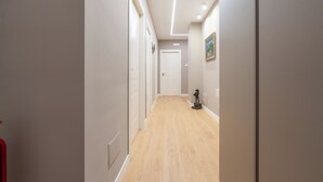 Um corredor com paredes claras, piso de madeira e uma porta branca no final.