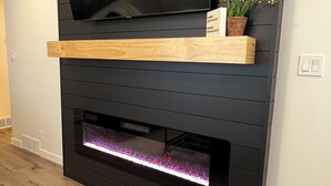 A modern entertainment unit with a flat-screen TV, wooden shelf, and built-in fireplace. - The Red Brick Retreat (Blackfoot)
