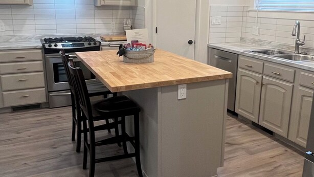 A modern kitchen with a central island, pendant lights, a stove, and a dishwasher. - The Red Brick Retreat (Blackfoot)