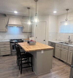 A modern kitchen with a central island, pendant lights, a stove, and a dishwasher.