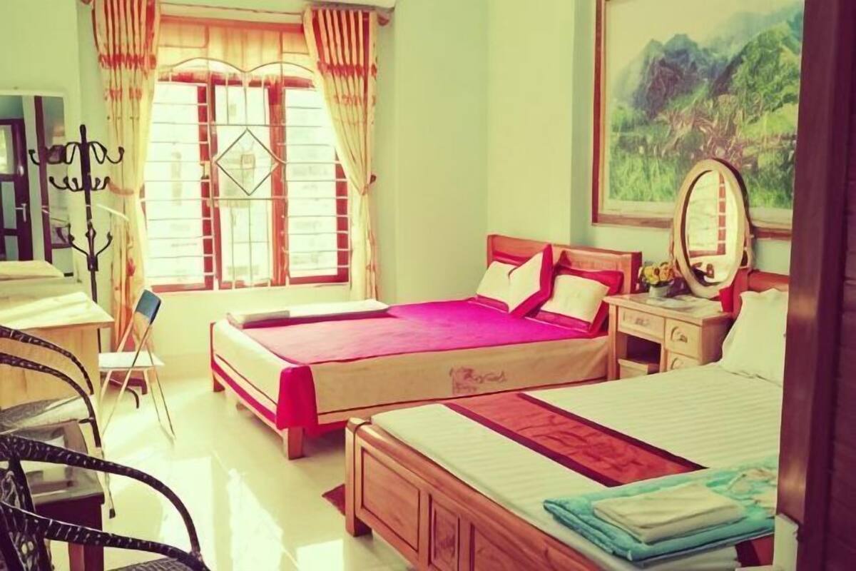 Una habitación con dos camas, un escritorio, una silla, un ventanal con cortinas y un cuadro en la pared.