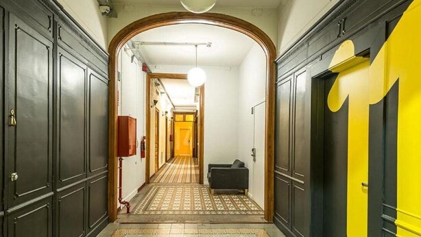 Un pasillo con puertas de madera oscura, alfombra estampada y una pared de acento amarilla.
