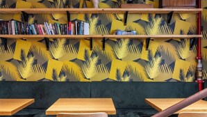 Un área de estar con mesas y sillas de madera, una estantería con libros y un pared con diseño.
