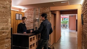 Un área de recepción con un mostrador de madera, un hombre de pie junto al mostrador y una mujer sentada detrás.