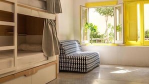 Habitación tipo dormitorio con literas, una silla estampada y una ventana con contraventanas amarillas.