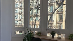 A room with a large window overlooking a building with balconies. There are two chairs and a potted plant on the windowsill. - Sweet BCN Youth Hostel (Barcelona)