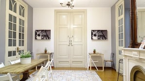 A room with a wooden dining table, white chairs, a chandelier, and two doors with glass panels. - Sweet BCN Youth Hostel (Barcelona)